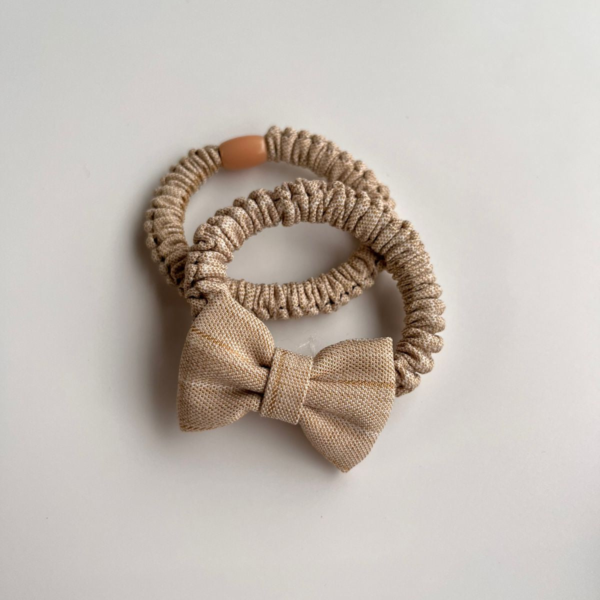 Set of beige hair scrunchies with a bow on a light gray background