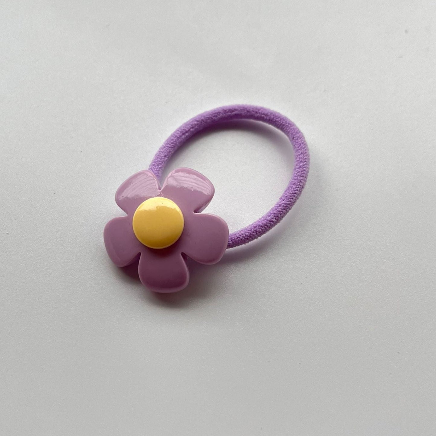 Purple flower-shaped hair tie on a light gray background