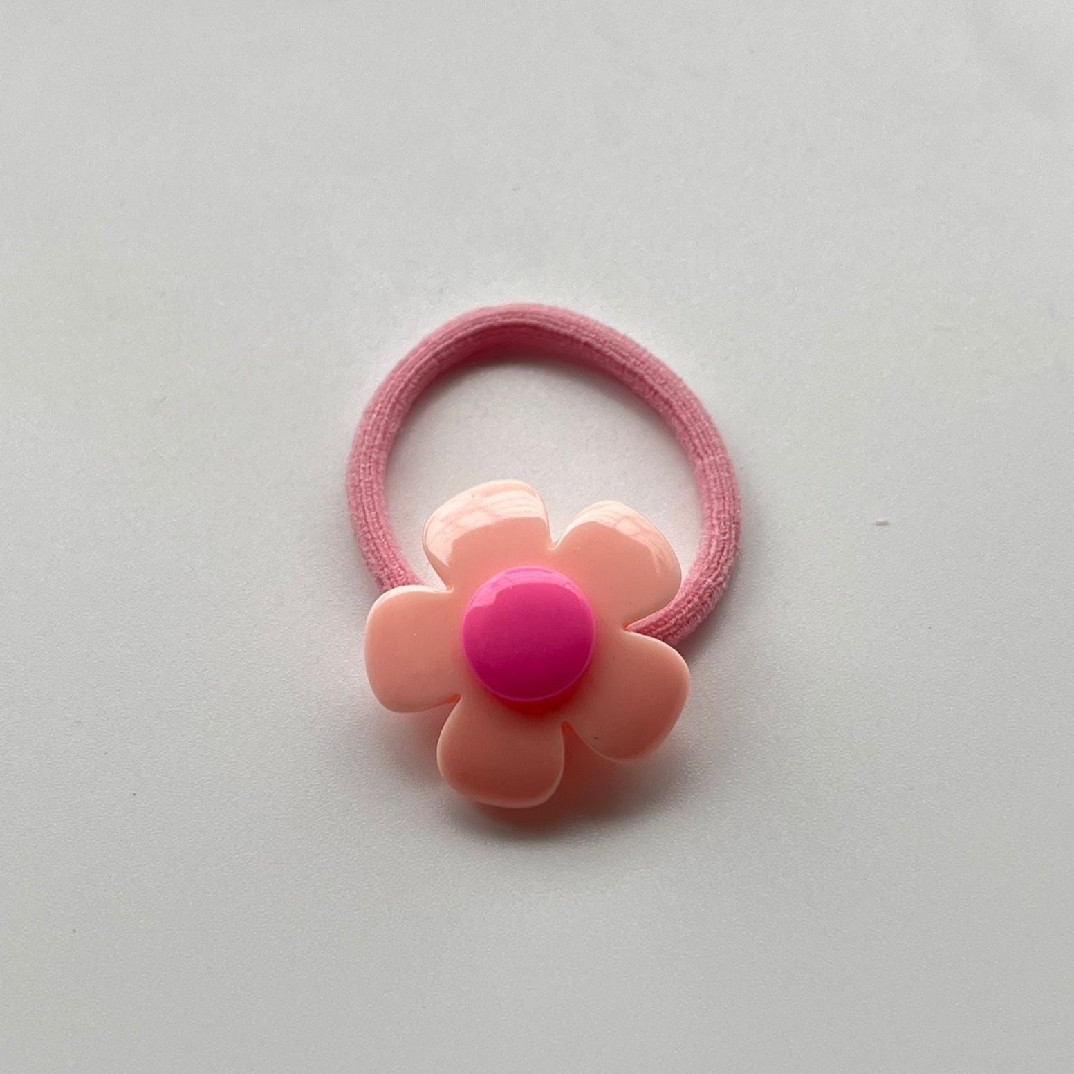Pink flower-shaped hair tie on a light gray background