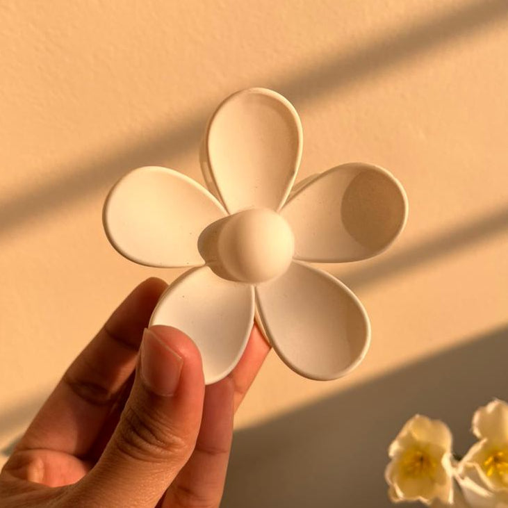 Hand holding a white ceramic flower against a warm-toned background