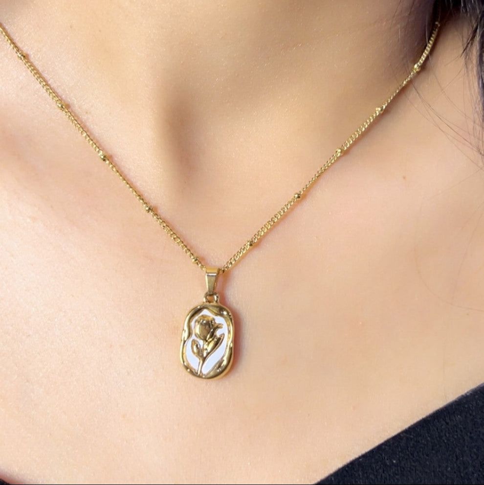 Gold necklace with a pendant featuring a rose design on a person's neck.