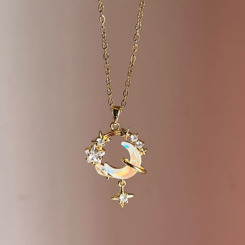 Delicate gold necklace with a moon and star pendant on a soft pink background