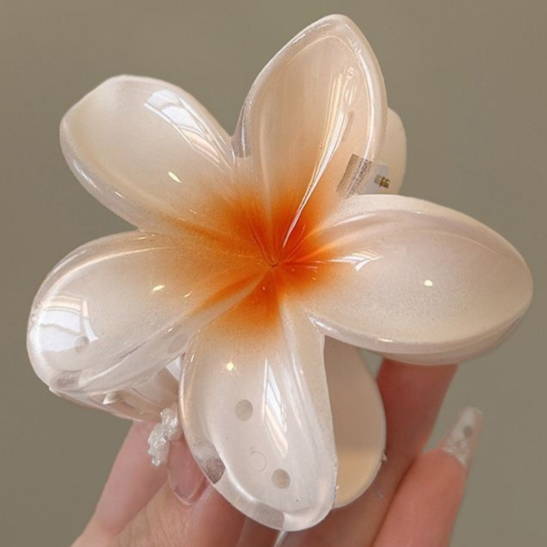 Hand holding a white and orange flower-shaped viral claw clip against a neutral background