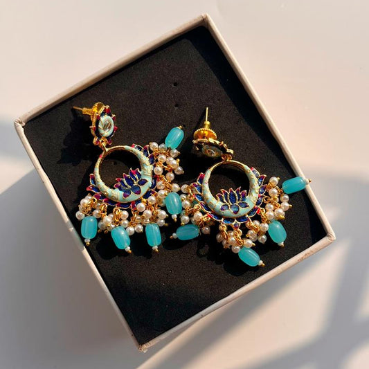 Pair of earrings with turquoise stones and gold accents in a box on a light background