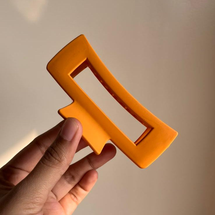 Hand holding an orange rectangular hair clip against a neutral background